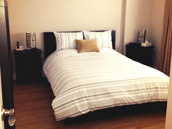 La chambre d’un appartement : lit à couette rayée, lampe de chevet, fenêtre