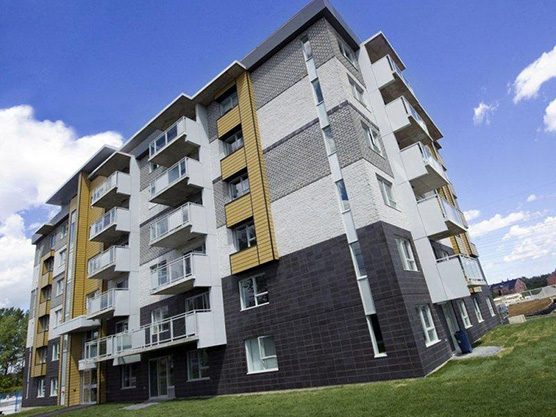 L’immeuble du Logix à Laval-des-Rapides : brique grise et noire, panneaux jaunes, balcons vitrés, ciel bleu