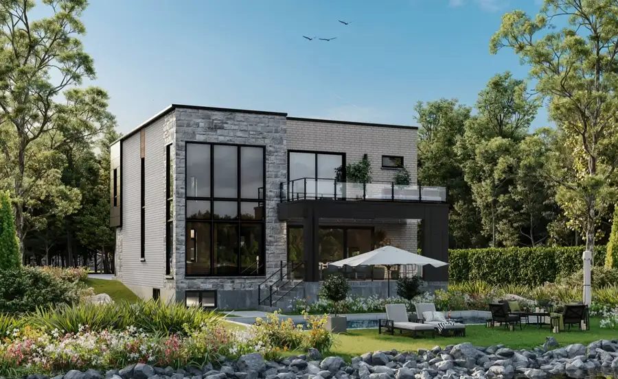La cour arrière de la maison modèle de la Terrasse Lafontaine, vue depuis la rivière des Prairies : terrasse couverte, balcon à l'étage, pelouse, plantations et berge de pierre