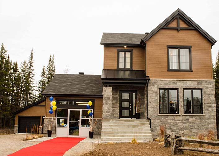 Un cottage de pierre et de bois à Sept-Îles, tapis rouge déroulé jusqu’à la porte, conifères derrière