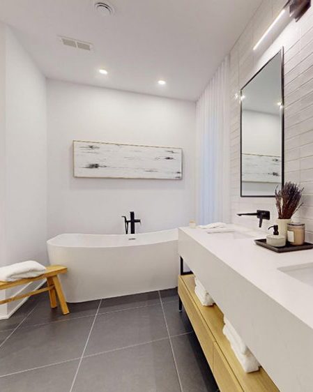 La salle de bain de la maison modèle : baignoire autoportante, douche vitrée, vanité de bois