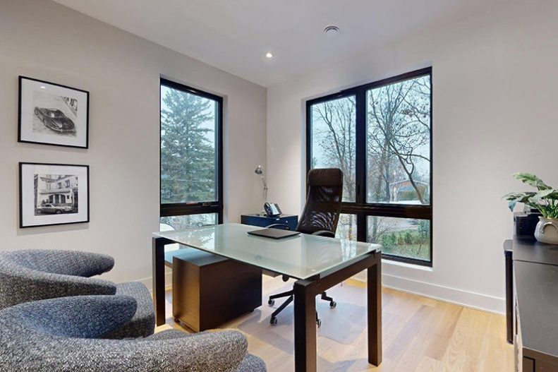 Le bureau de la maison modèle : table de verre, chaises grises, fenêtres noires sur les arbres