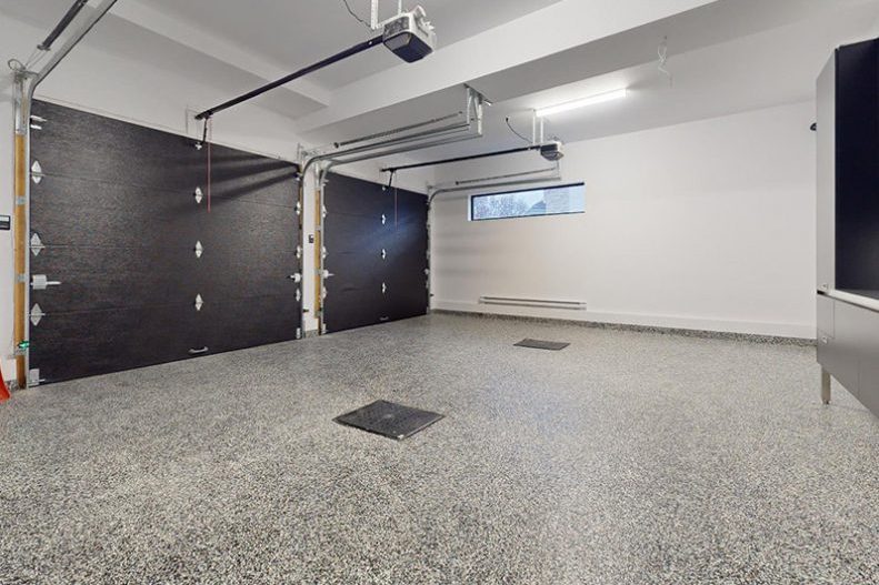 Le garage double de la maison modèle, plancher d’époxy moucheté et portes noires