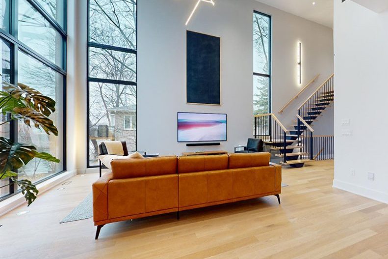 Le mur de fenêtres du salon sur deux étages, canapé cognac devant, arbres dehors