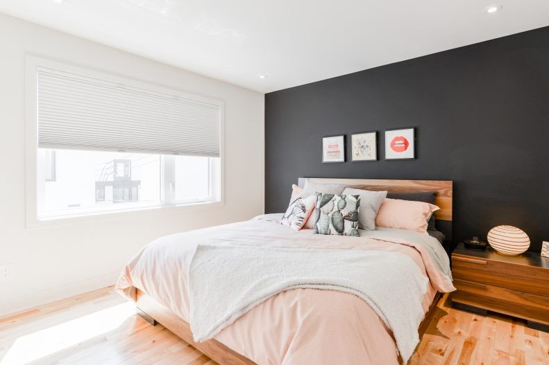 Une chambre : lit de bois, mur anthracite, literie rose pâle, cadres au mur