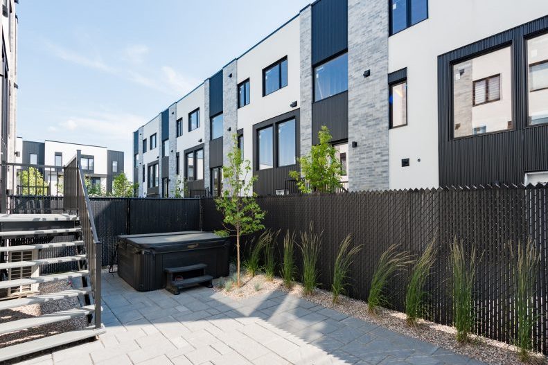 Une autre cour arrière : spa, escalier de métal, terrasse de pavés gris, arbustes