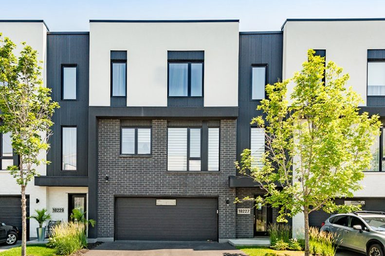 Une rangée de maisons de ville des Villas Cité Mirabel : façades noires et blanches, brique, garages, jeunes arbres