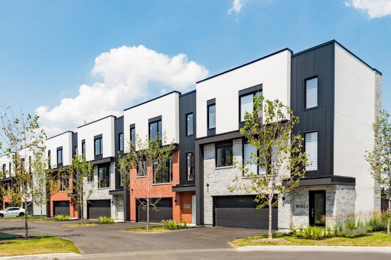 Rangée de maisons de ville sous un ciel de nuages, garages noirs, jeunes arbres