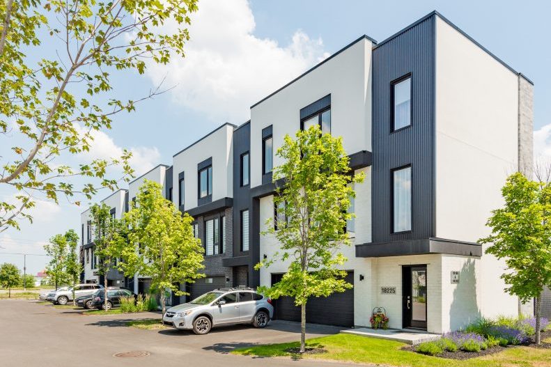 Une rangée de maisons de ville noires et blanches vue de la rue, voitures stationnées, ciel bleu